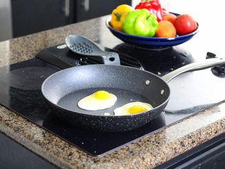 The non-stick Bialetti Titan Fry Pan on a countertop stove, cooking eggs with fresh produce on the counter beside it.