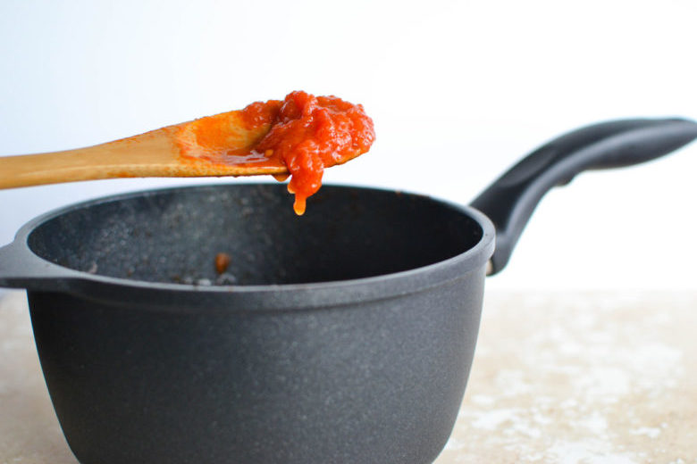The Swiss Diamond sauce pan with a spoonful of tomato sauce held above it
