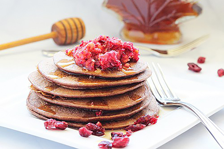 A stack of Dark Chocolate Cranberry Protein Pancakes with fresh raspberries on top
