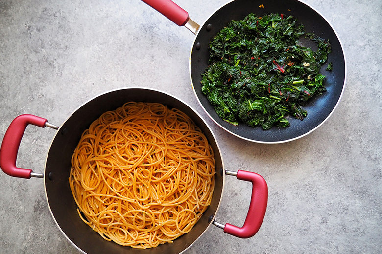 Greens in a pot and pasta in a larger two-handled pot, shot from above