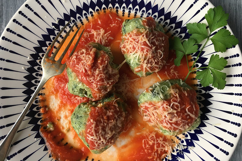 Spinach and Ricotta Malfatti, covered in tomato sauce and grated Parmesan cheese, shot from above. This meal is on a black and white patterned plate and garnished with a sprig of herb