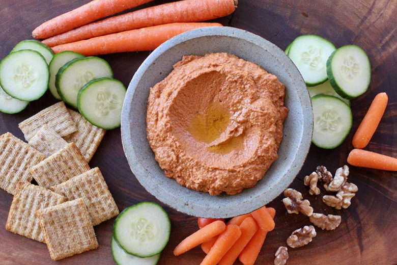 Red pepper walnut dip in a bowl surrounded by crackers, vegetables and more