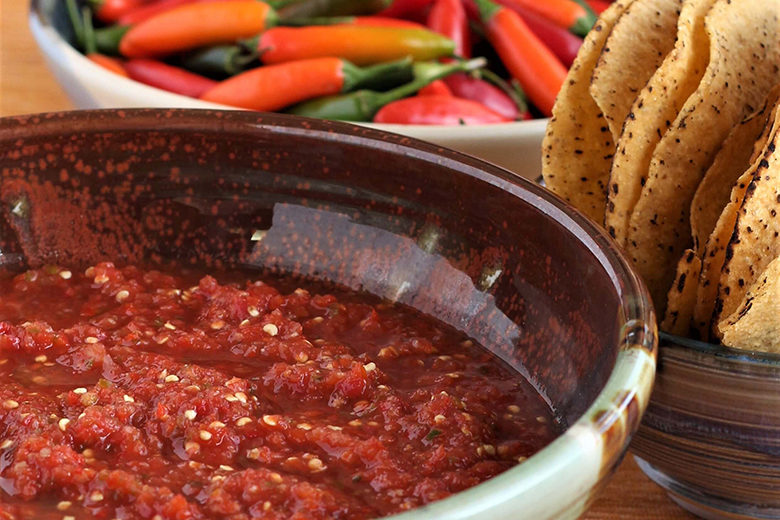 A bowl of salsa next to a bowl of chiles and tortilla chips