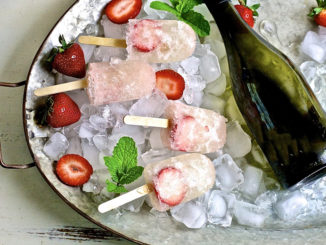 Strawberry prosecco pops in a bowl of ice with fresh strawberries and a bottle of prosecco nearby