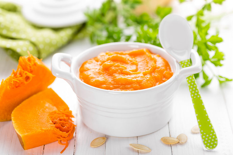 Bowl of baby food with pumpkin and herbs on white table