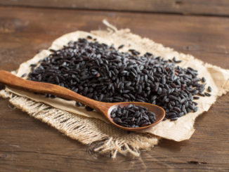 Pile of black rice with a spoon on a wooden table
