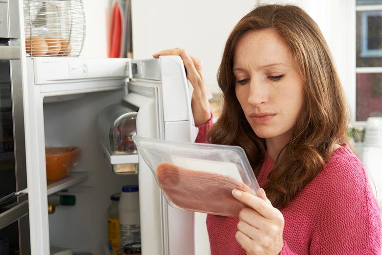Woman looking at label of lunch meat with fridge open