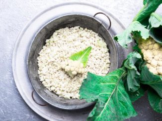 Cauliflower "rice" in a metal pan with fresh greens around it