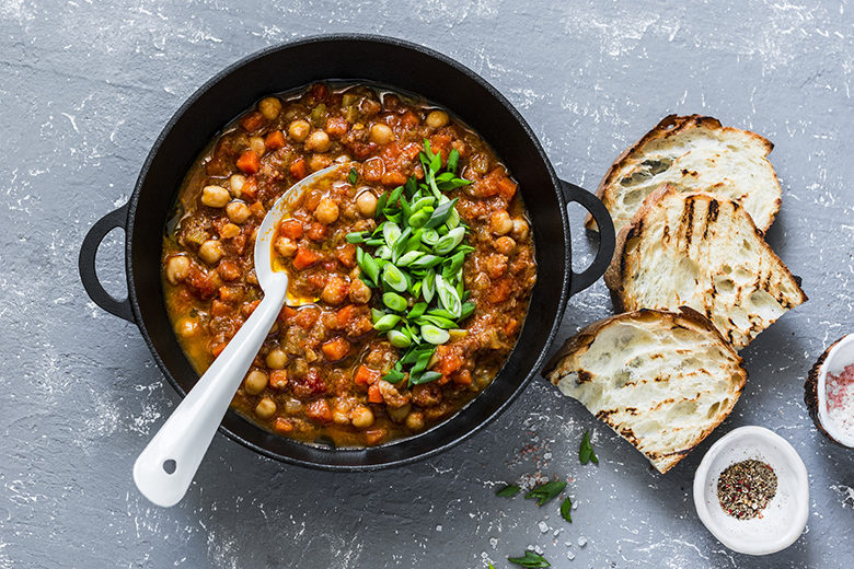 Vegetarian mushrooms chickpea stew in a iron pan and rustic grilled bread on a gray background, top view. Healthy vegetarian food concept