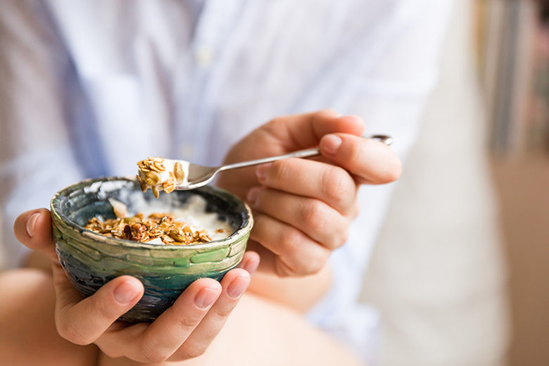 Young woman with muesli bowl. Girl eating breakfast cereals with nuts, pumpkin seeds, oats and yogurt in bowl. Girl holding homemade granola. Healthy snack or breakfast in the morning.