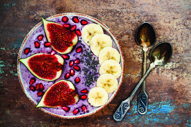 Healthy fall and winter breakfast set. Acai superfoods smoothies bowl with chia seeds, pomegranate, sliced banana, fresh figs and hazelnut butter.
