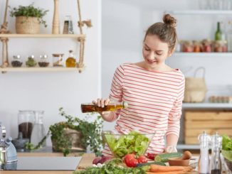 Woman in kitchen pouring oil onto salad greens