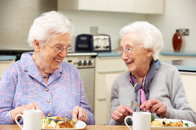 Senior women enjoying meal together in kitchen at home