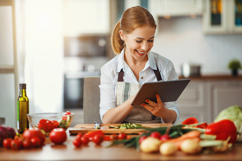 happy woman preparing vegetables in kitchen on prescription with tablet
